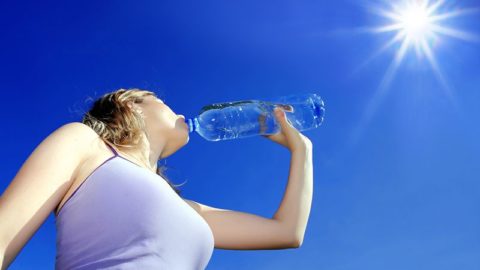 Mulher bebendo água mineral engarrafada sob o sol
