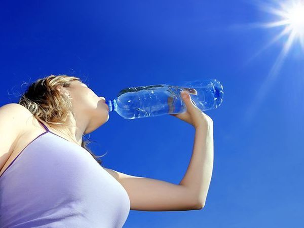 Mulher bebendo água mineral engarrafada sob o sol